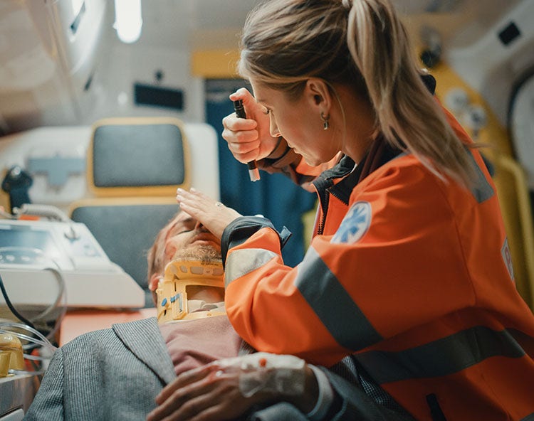 A female paramedic in an ambulance checking on a male patient with a neck brace and a head injury.